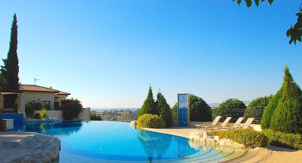 A swimming pool with a view of the landscape, a building with a tiled roof, and a tall tree. - Junior Villa EZ02 - Minimi (Kouklia)