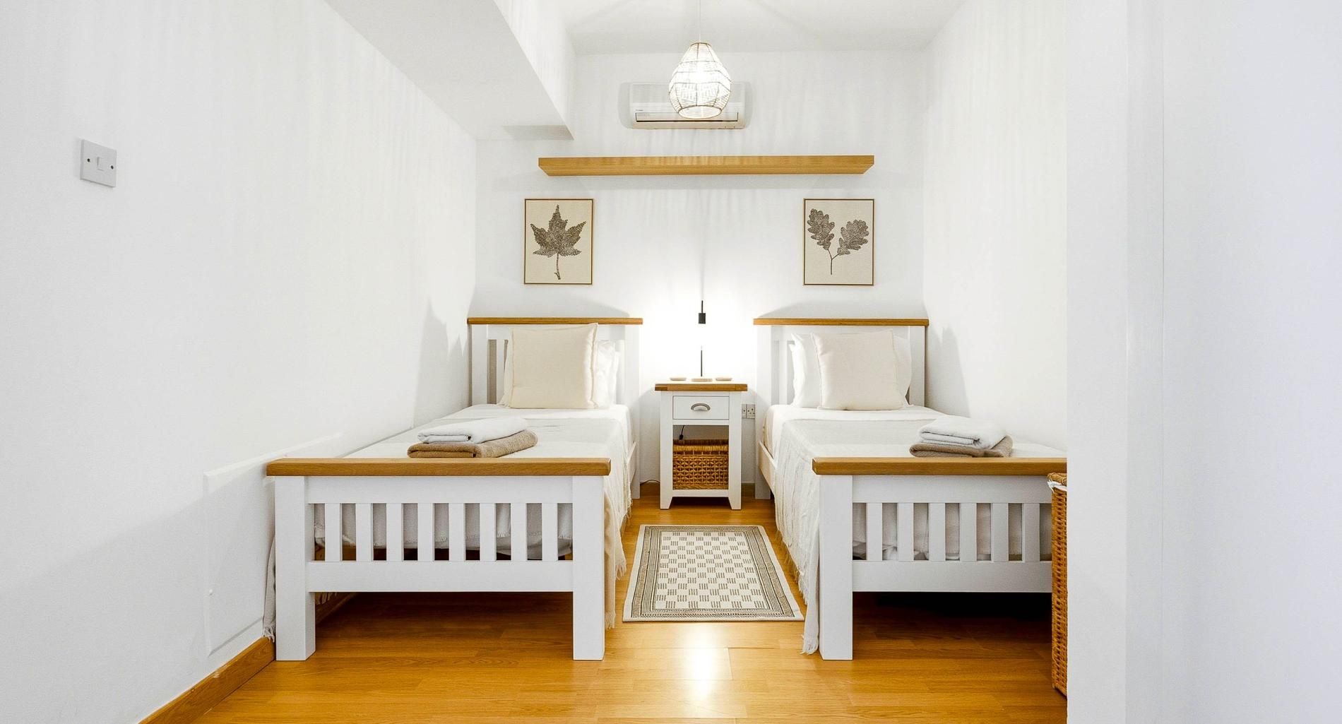 Une chambre avec deux lits simples, une petite table de chevet avec une lampe, un ventilateur de plafond et un climatiseur fixé au mur.