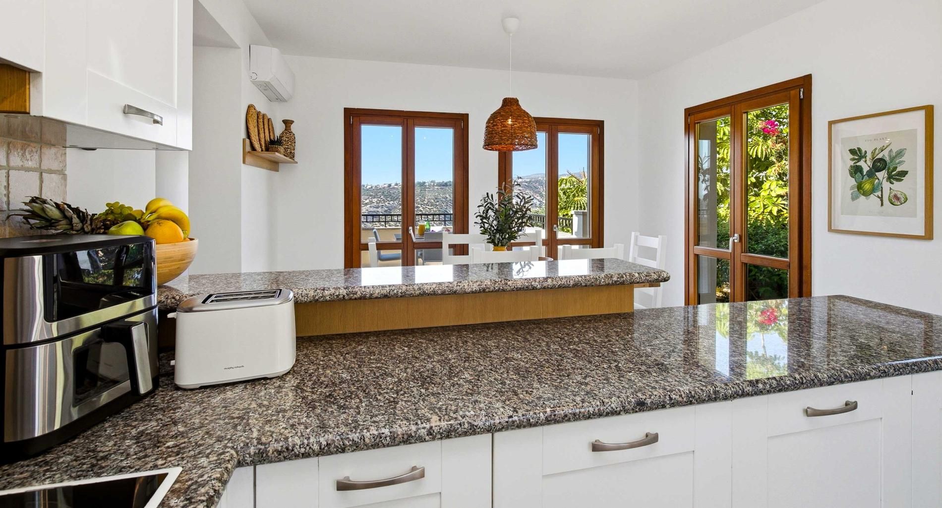 Una cocina moderna con encimeras de granito, electrodomésticos de acero inoxidable y vistas al exterior a través de amplias ventanas.