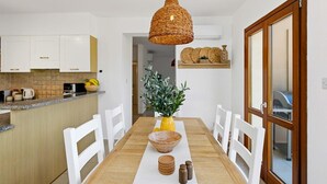 A kitchen with white cabinets, a wooden countertop, a dining table with white chairs, a hanging wicker light fixture, and a potted plant. - Junior Villa EZ02 - Minimi (Kouklia)