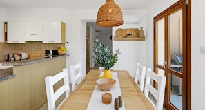 A kitchen with white cabinets, a wooden countertop, a dining table with white chairs, a hanging wicker light fixture, and a potted plant. - Junior Villa EZ02 - Minimi (Kouklia)