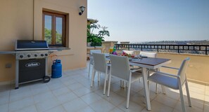An outdoor patio with a grill, dining table, chairs, and a view of the sea. - Junior Villa EZ02 - Minimi (Kouklia)