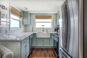 Cocina compacta con una isla central, horno empotrado y refrigerador de acero inoxidable.