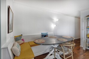 Ein Zimmer mit einem runden Tisch, zwei Stühlen, einer Bank mit Kissen, einer Wandlampe und einem Bücherregal.
