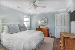 Ein Schlafzimmer mit Bett, Kommode, Spiegel, Deckenventilator und einer Tür.