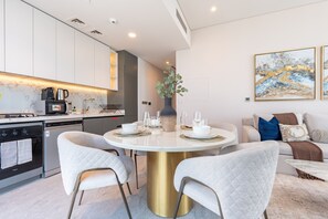 A modern kitchen with built-in appliances, a dining area with a round table, and a living room with a sofa and decorative pillows. - 40th+ Floor 1BR w/ Burj Khalifa & Canal Views, Spacious Balcony, Near Downtown (Dubai)