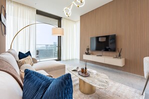 A modern living room with a sofa, coffee table, and a television mounted on a wooden wall. - 40th+ Floor 1BR w/ Burj Khalifa & Canal Views, Spacious Balcony, Near Downtown (Dubai)