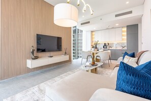 Ein modernes Wohnzimmer mit einem Flachbildfernseher, einem Essbereich mit einem runden Tisch und einer Küche mit weißen Schränken.