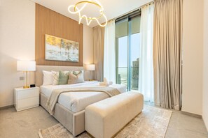 A modern bedroom with a large bed, bedside lamps, a painting, and a view of a cityscape through the window. - 40th+ Floor 1BR w/ Burj Khalifa & Canal Views, Spacious Balcony, Near Downtown (Dubai)