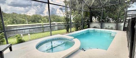 A swimming pool with a hot tub, surrounded by a glass enclosure, with a view of trees and a cloudy sky.