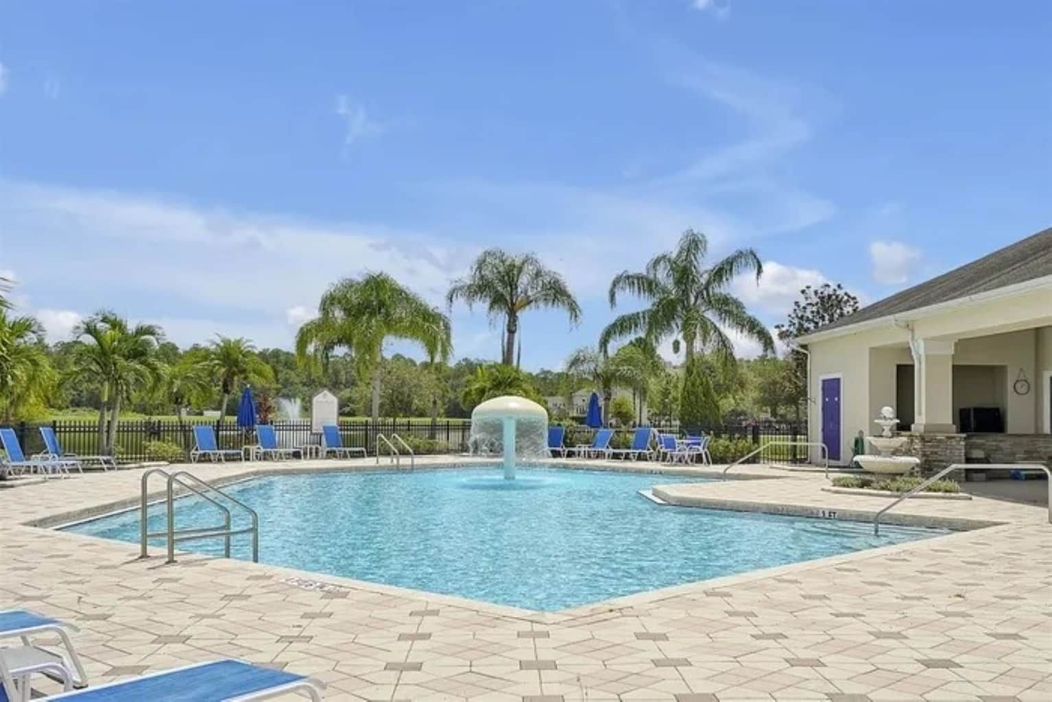 Une piscine agrémentée d’un élément décoratif aquatique au centre, entourée de chaises longues et de palmiers.