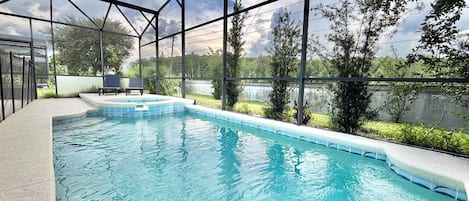 An indoor swimming pool with clear glass walls, a hot tub, and a seating area with chairs.