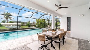 A poolside dining area with a table and chairs, a ceiling fan, and a view of the pool and surrounding landscape. - Ref 426. 4 Bedromm Cape Coral waterfront villa. Own pool (Cape Coral)