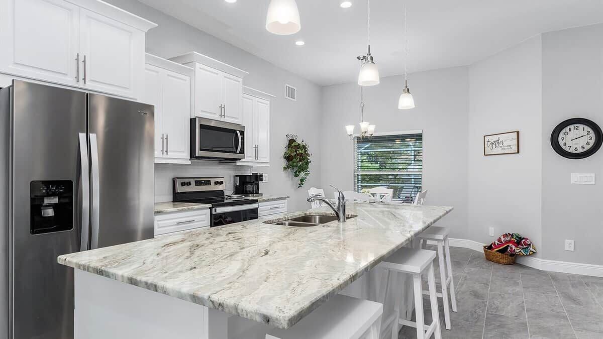 A modern kitchen with white cabinetry, stainless steel appliances, and a marble countertop.