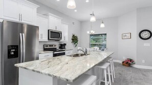 Uma cozinha moderna com armários brancos, eletrodomésticos de aço inoxidável e bancada de mármore.