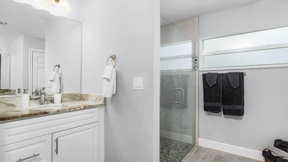 Un baño moderno con cabina de ducha de vidrio, encimera de mármol y muebles de color blanco.