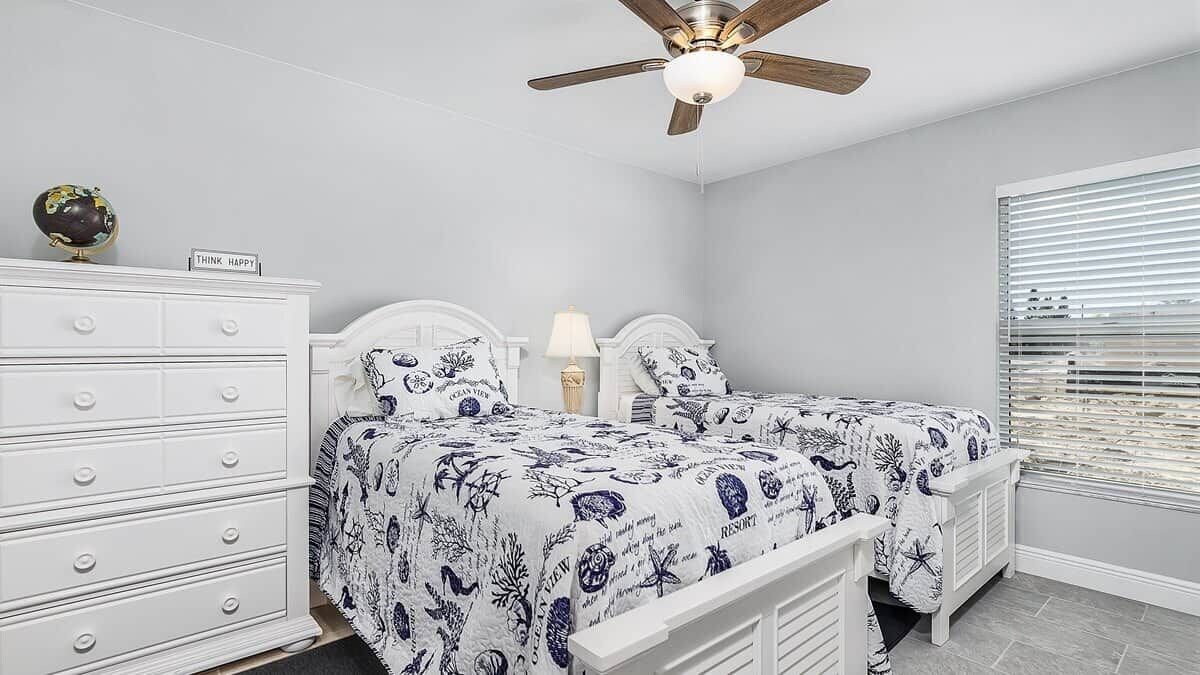 Une chambre avec deux lits, une commode, un globe terrestre et un ventilateur de plafond.