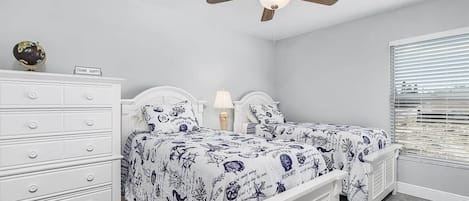 A bedroom with two beds, a dresser, a globe, and a ceiling fan.