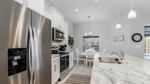 Een moderne keuken met roestvrijstalen apparatuur, een marmeren aanrecht en een eethoek met witte stoelen.