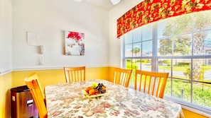 Comedor con una mesa lista para dos personas, frutero y vistas al exterior.