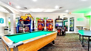 Ein Billardtisch mit Spielautomaten im Hintergrund, ein Tischtennistisch und ein Hinweisschild für den Ausgang.