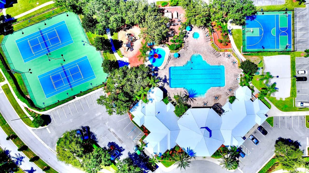 An aerial view of a sports complex with tennis courts, a swimming pool, and a parking area.