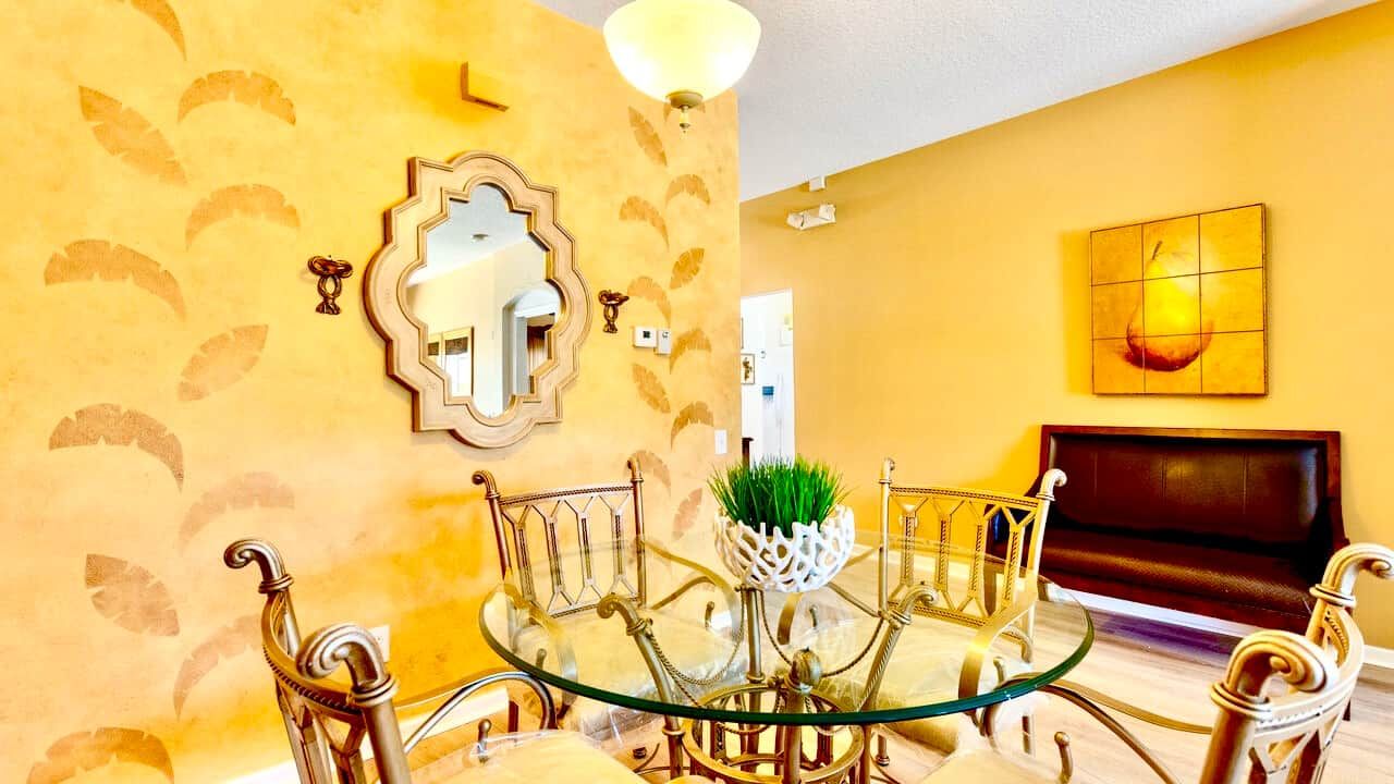 A dining area with a glass table, ornate chairs, a decorative mirror, and a painting on the wall.