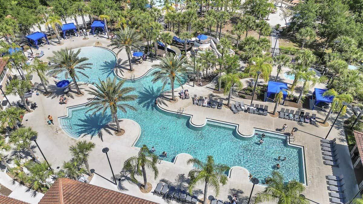 A large outdoor swimming pool surrounded by palm trees and lounge chairs.