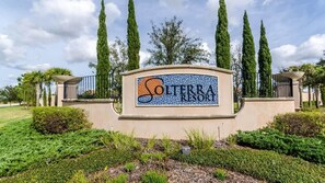 Schild für Solterra Resort mit Kachelmuster, umgeben von Grünpflanzen und hohen Bäumen.