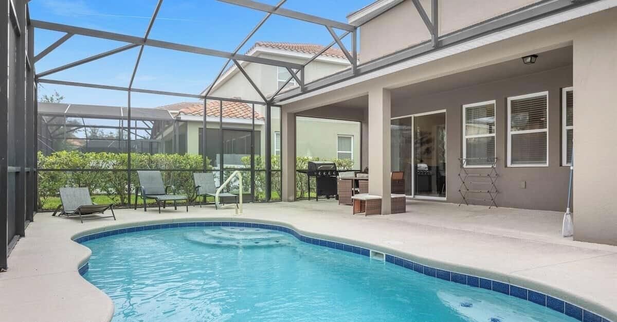 Una piscina con cerramiento de vidrio, mobiliario exterior y un patio cubierto.