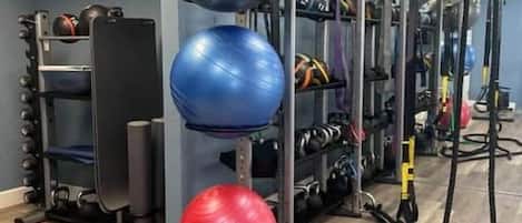 Un gimnasio con equipo de ejercicio, que incluye una jaula para sentadillas, balones medicinales y un banco.