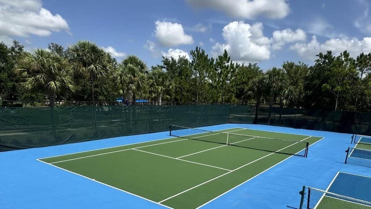 Una cancha de tenis con una red, rodeada por una valla verde y árboles.