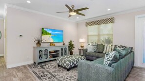 A living room with a television, a ceiling fan, a sofa, an ottoman, and a patterned rug. - ref 900. 4 bedroom Cape Coral waterfront villa. Own pool (Cape Coral)