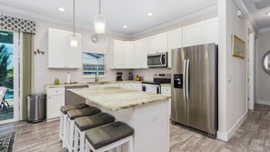 Una cocina moderna con armarios blancos, electrodomésticos de acero inoxidable y una isla central con asientos.