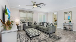 A modern living room with a grey sectional sofa, a patterned ottoman, a ceiling fan, a TV, and a decorative plant. - ref 900. 4 bedroom Cape Coral waterfront villa. Own pool (Cape Coral)