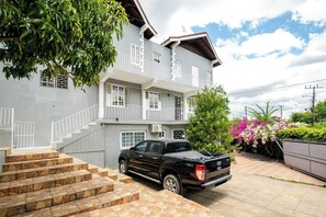 A two-story building with a staircase leading to the entrance, a parked pickup truck, and a garden with flowering plants. - The hillls - Beverly Hills overlooking Kingston (Kingston)