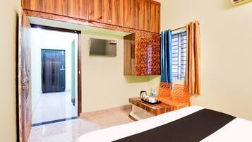 A hotel room with a bed, a bedside table with a kettle and water bottles, a mirror, and a window with curtains.