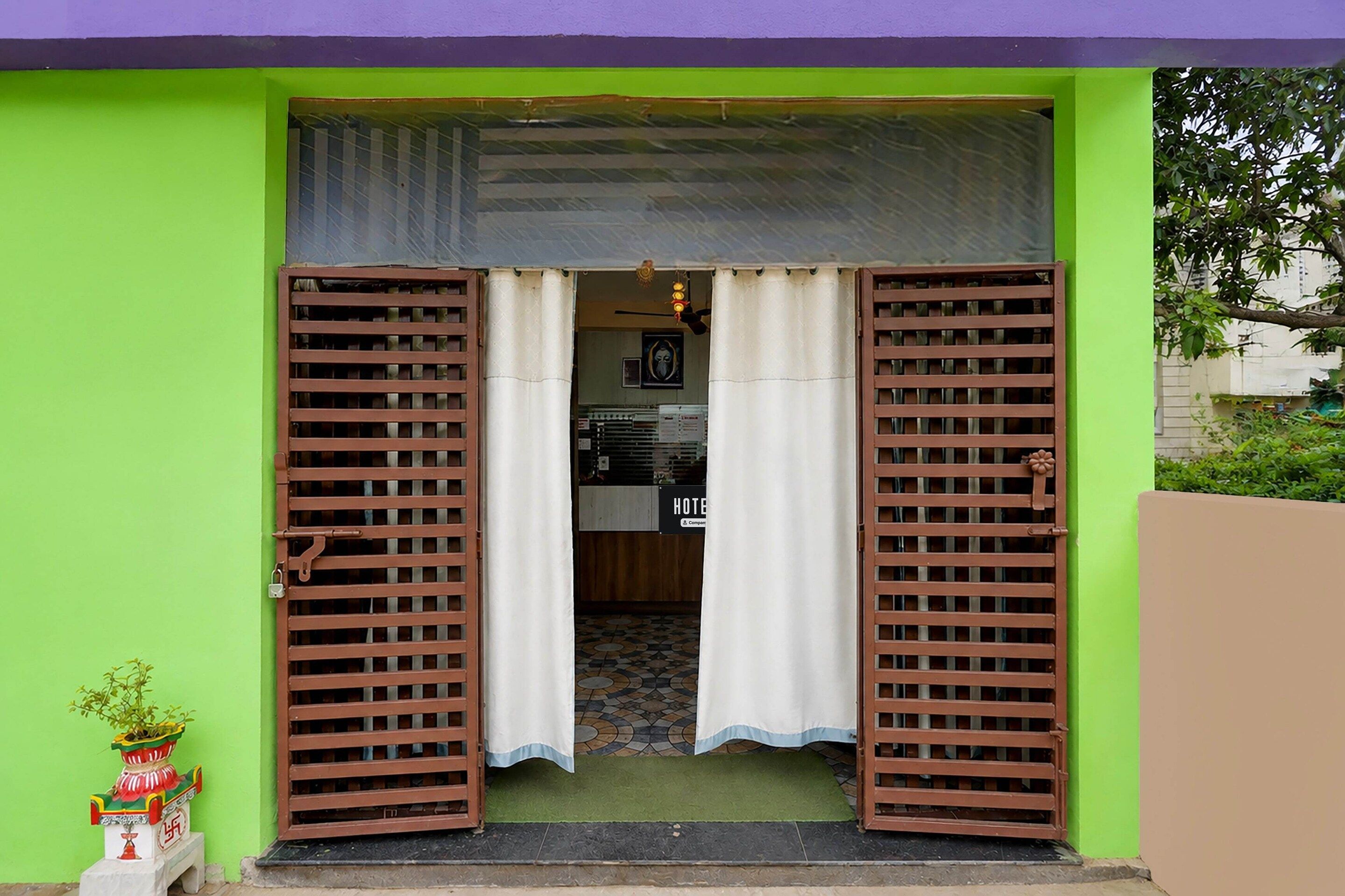 A hotel entrance with a green facade, a tiled entrance, and a sign indicating the hotel's name.