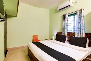 Une chambre d’hôtel avec un lit, une chaise, une table de chevet, une lampe et une fenêtre avec des rideaux.