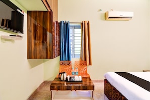 A hotel room with a bed, a wooden desk with a kettle and Bisleri water bottles, a TV, and an air conditioner. - Deluxe Room Star Light (Bhubaneshwar)