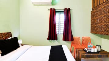 Una habitación de hotel con una cama, una mesita de noche, una mesa con hervidor y botellas de agua, y un aire acondicionado instalado en la pared.