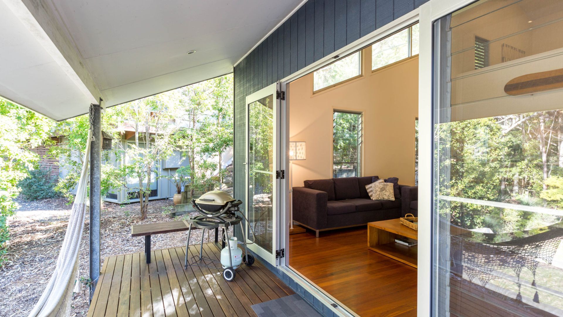 A modern living room with a dark sofa, a wooden coffee table, and a hammock outside.
