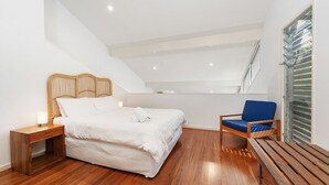 Quarto com cama, mesa de cabeceira, cadeira e janela com persianas.