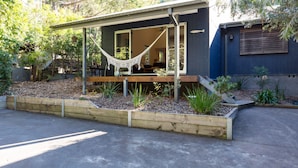 A modern house with a hammock on the porch, wooden deck, and a garden with various plants.