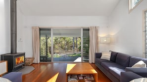 Un salon moderne doté d’une cheminée, d’un canapé, d’une table basse et offrant une vue sur un hamac et des arbres, le tout visible à travers de grandes portes vitrées.