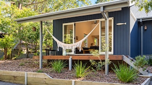 A modern house with a wooden deck, a hammock, and a garden with various plants. - Boathouse 1 by Experience Jervis Bay (Hyams Beach)