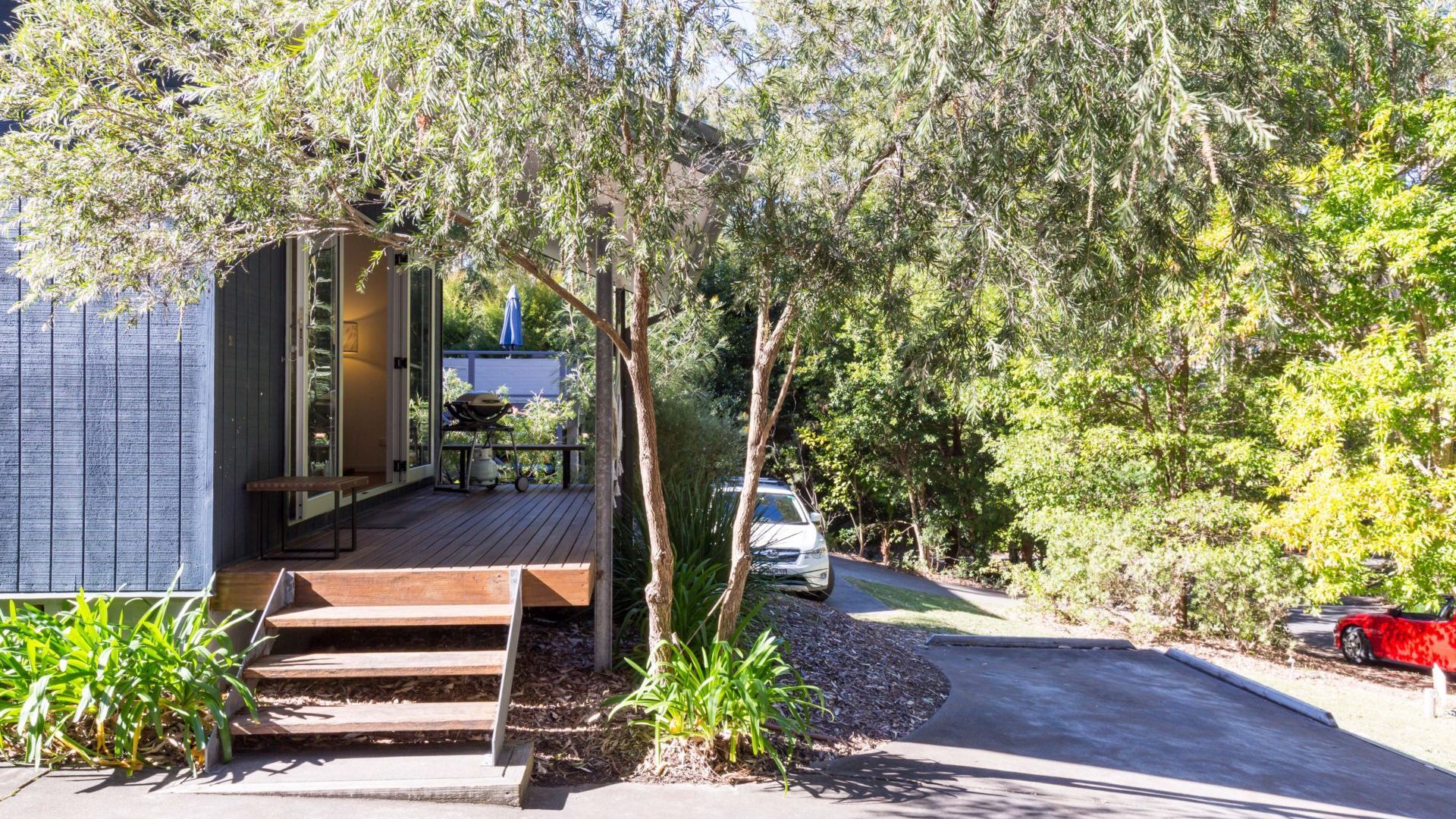 A modern house with a wooden deck, a barbecue setup, and a car parked in the driveway.