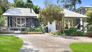 Uma casa de dois andares com um amplo jardim frontal, uma rede e diversas plantas.