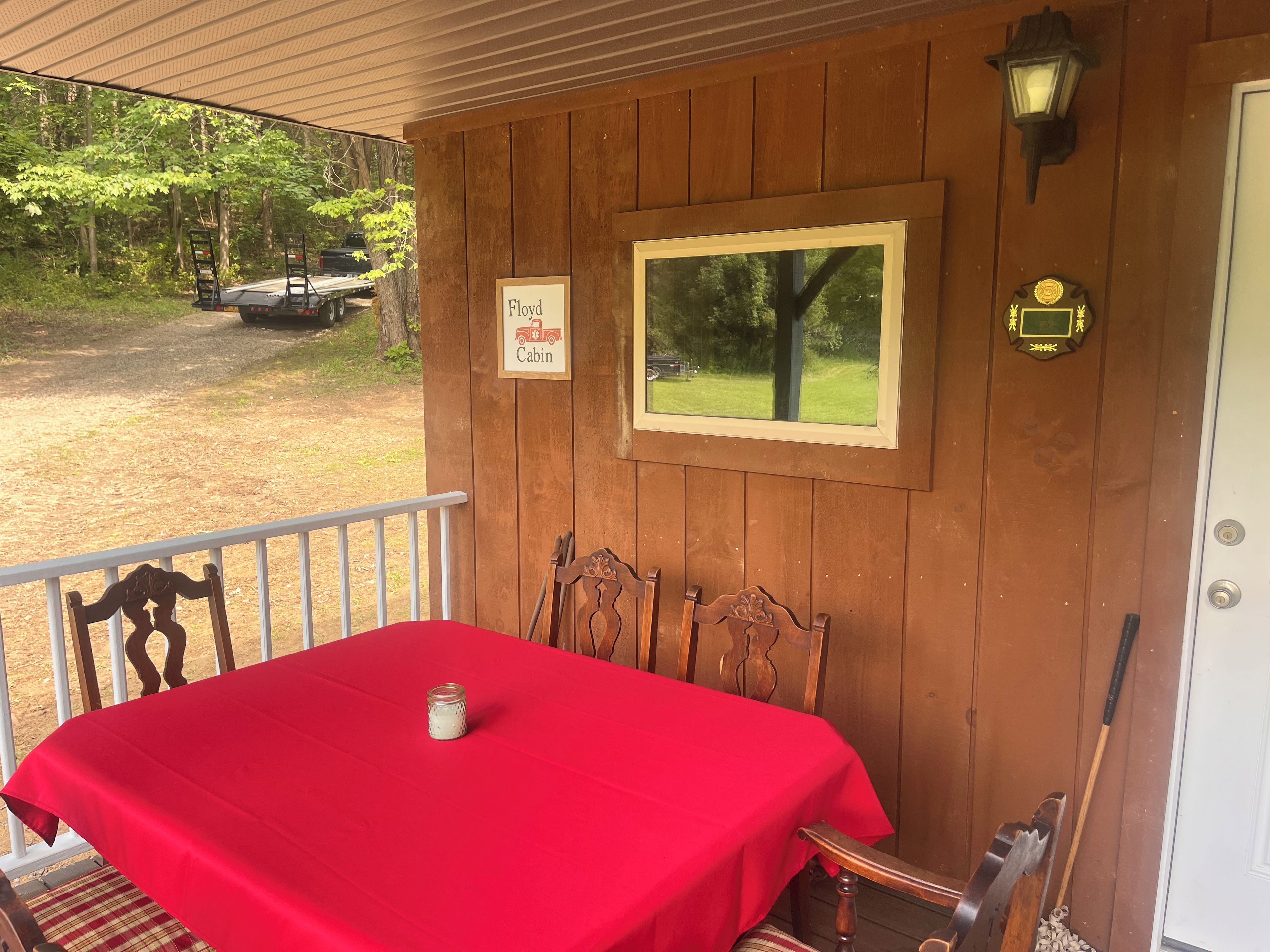 Une cabane en bois avec une table rouge, deux chaises, une pancarte indiquant « Cabane de Floyd », un tableau encadré et une porte ornée de blasons.