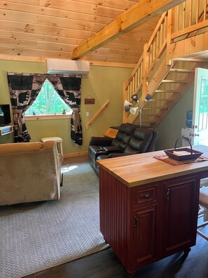 A cozy living room with a wooden ceiling, a sofa, a leather chair, and a desk with drawers. - Floyd cabin (Dansville)